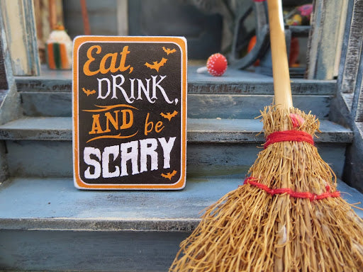 A witch’s broom resting on a staircase next to a sign that says “Eat, drink, and be scary