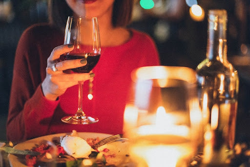 A woman in a red shirt holding a glass of red wine at a dinner table