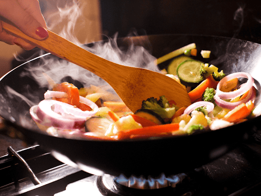 Close-up of a hand mixing vegetables in a wok for a vegan stir fry