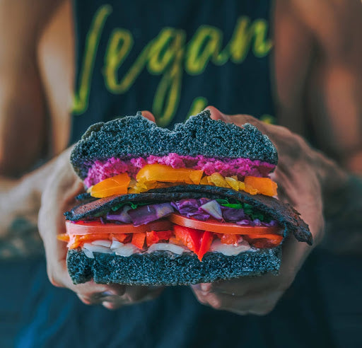 A man wearing a shirt that says “Vegan” holding a sandwich with all vegan ingredients