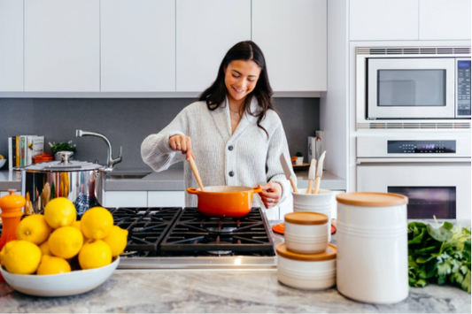 A smiling woman stirring a pot on a hot stovetop