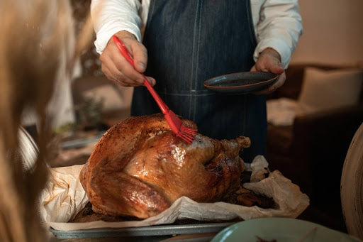 A man brushes a large chicken with a pepper jelly glaze