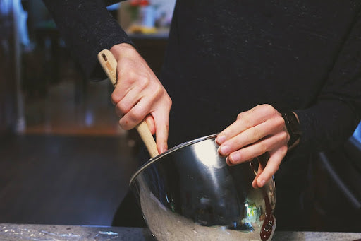 Close-up of a cook’s hands as they mix a homemade pepper jelly glaze in a metal bowl