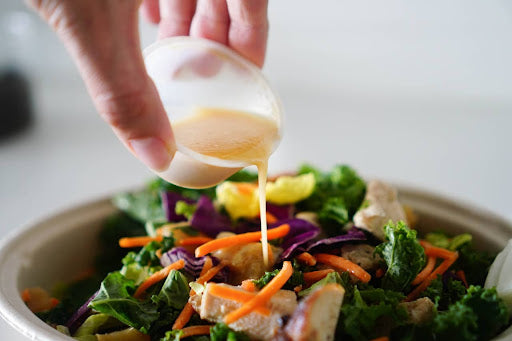 Close-up of a cup of dressing being poured onto a salad