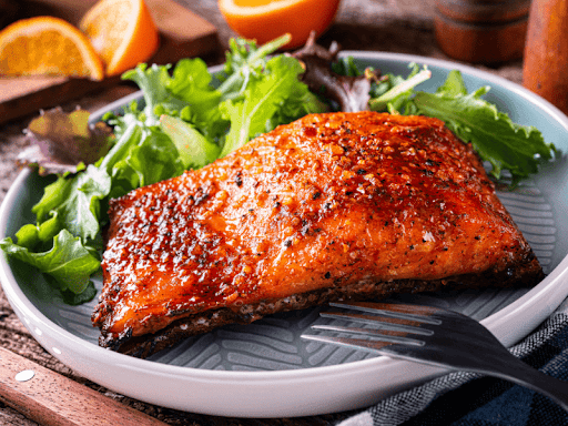 Close-up of a plate of spicy glazed salmon with a wide of mixed greens for garnish