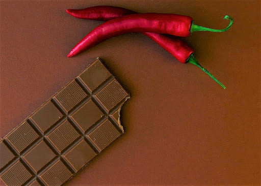 A partially eaten chocolate bar sitting next to a pair of red chili peppers