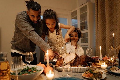 A father helping his young daughter carve the Thanksgiving turkey while her mother watches